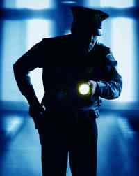 A security guard in a dark room with his flashlight on.